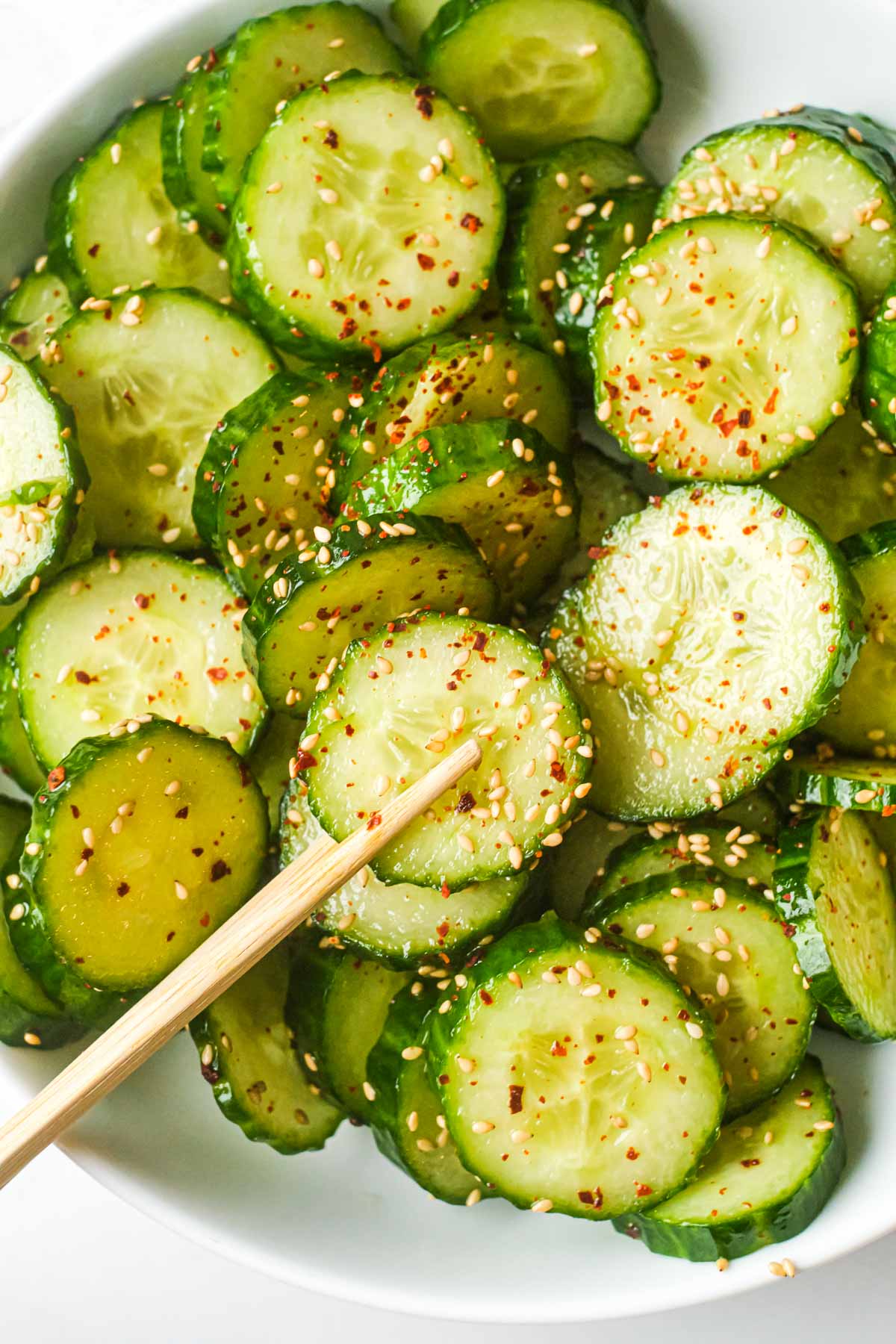top down view of the completed asian cucumber salad with chopsticks removing one slice of cucumber