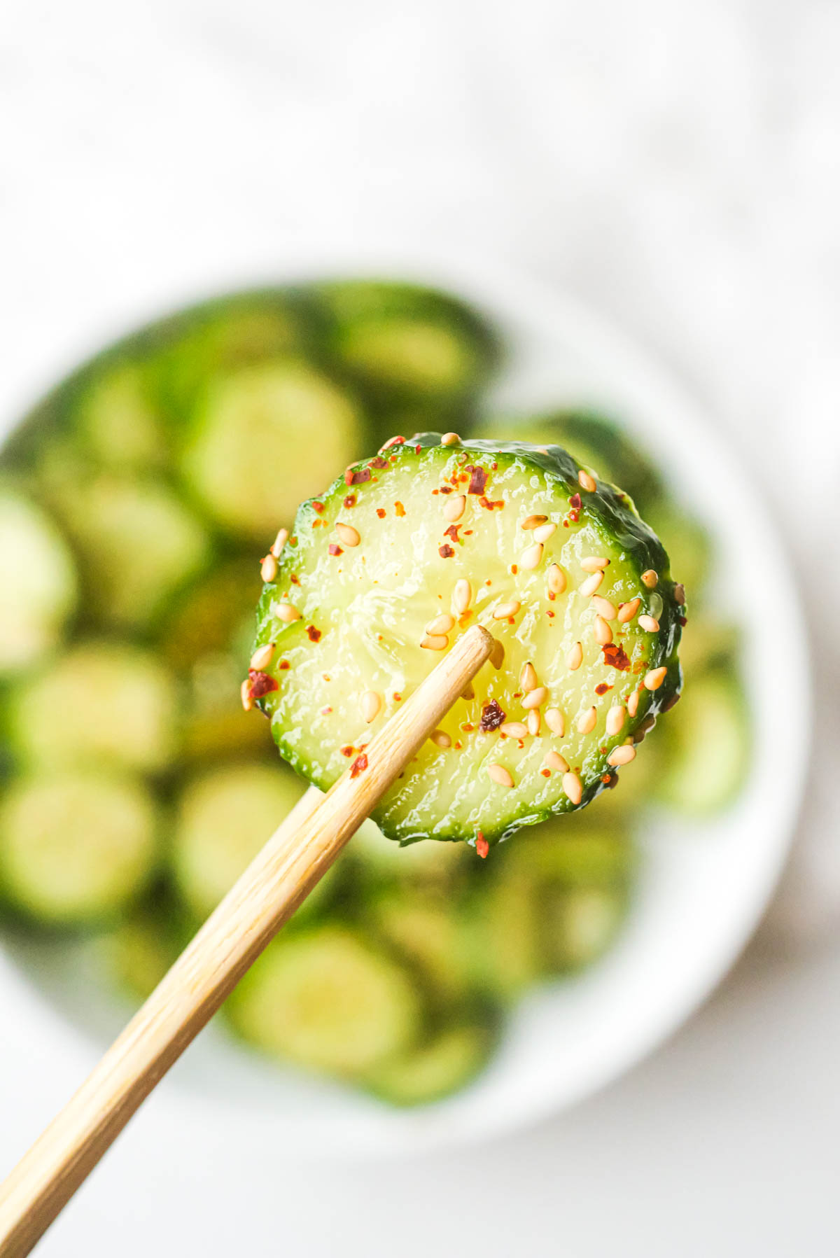 close up view of a single slice of cucumber that was removed from the asian cucumber salad being held with chopsticks