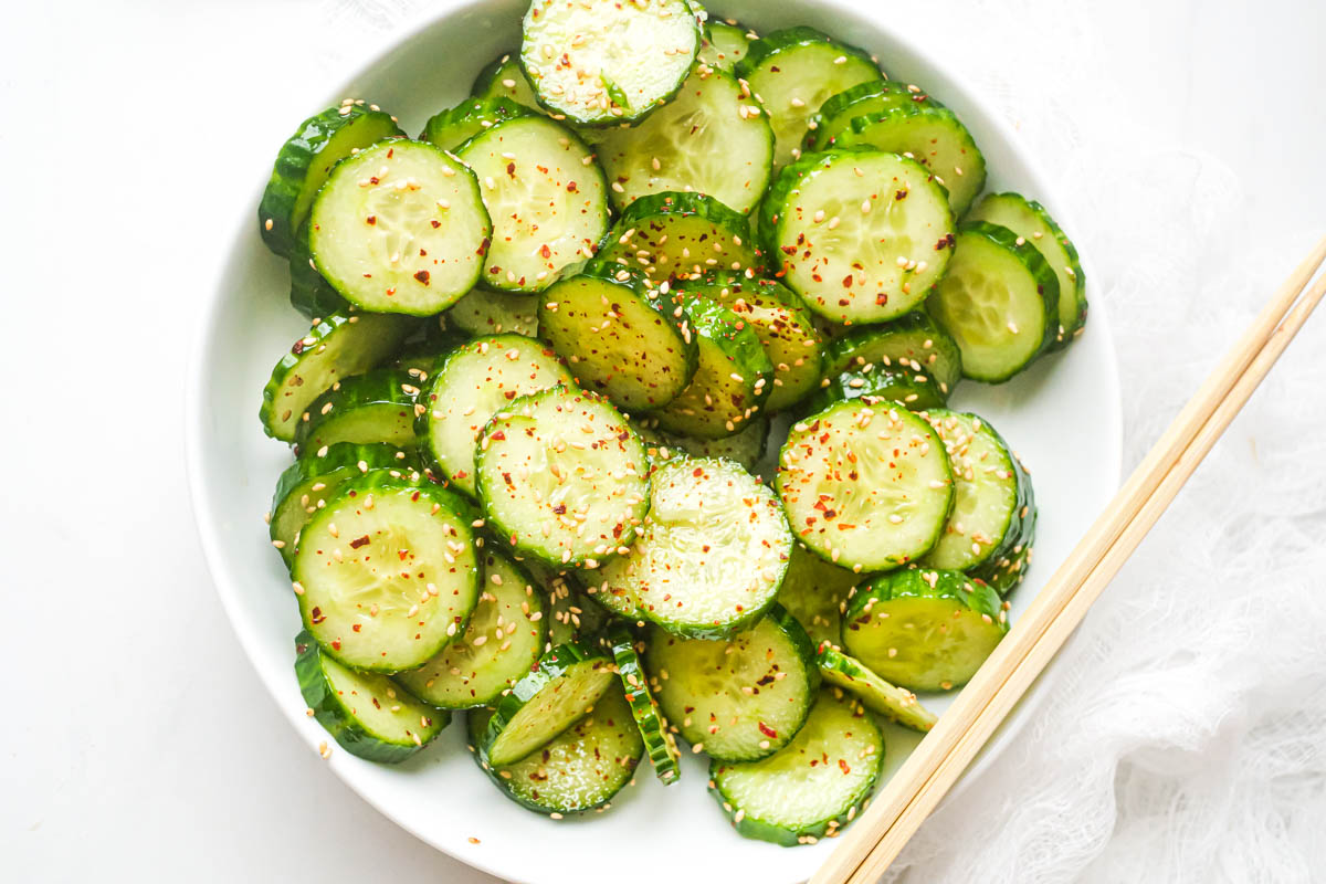 a bowl filled with asian cucumber salad with chopsticks placed across the edge