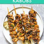 four chicken skewers on a plate with a lime garnish