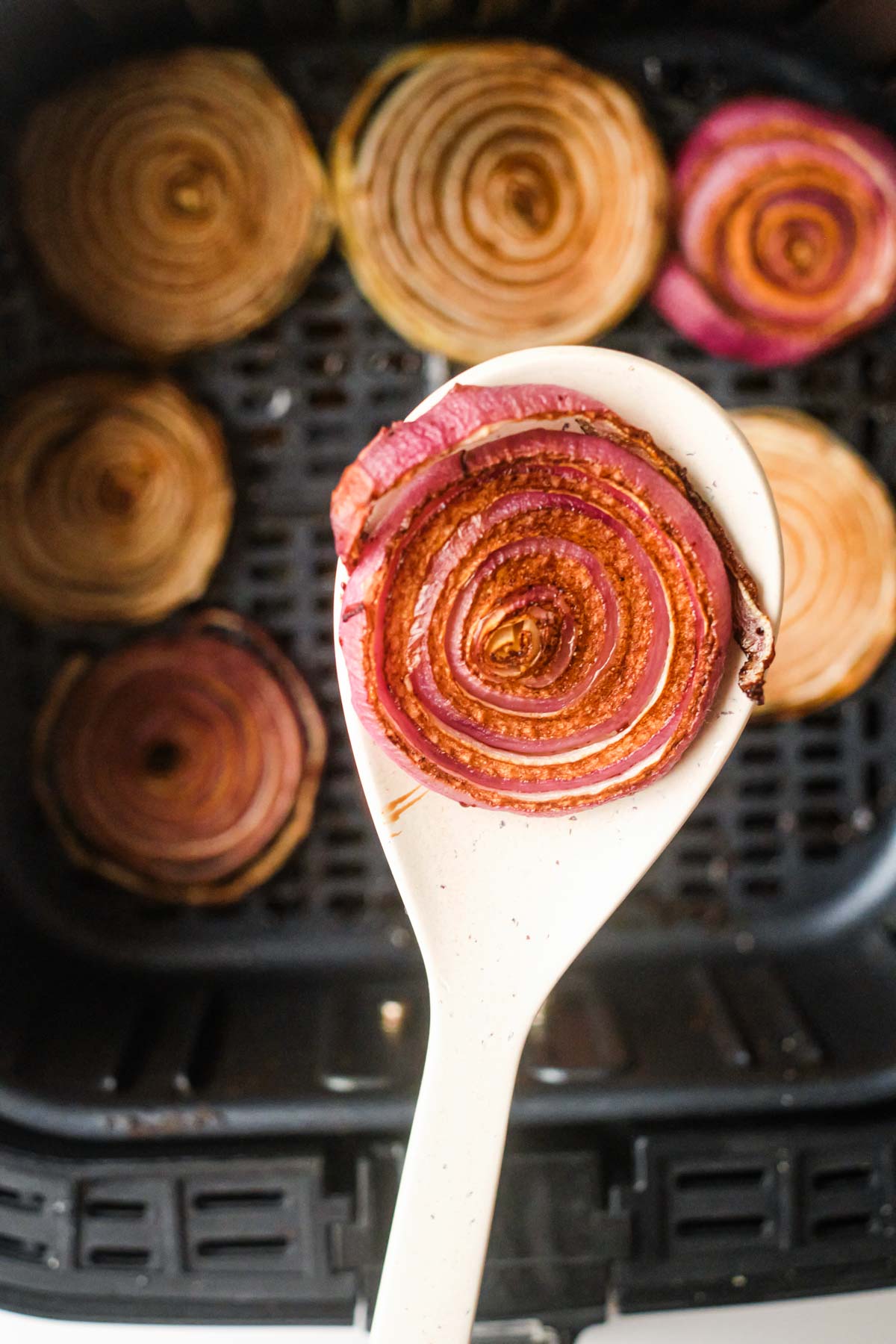 close up of a wooden spoon removing one portion of air fryer onions from the air fryer basket