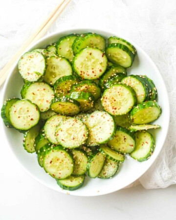 one serving of asian cucumber salad in a white bowl with a pair of chopsticks