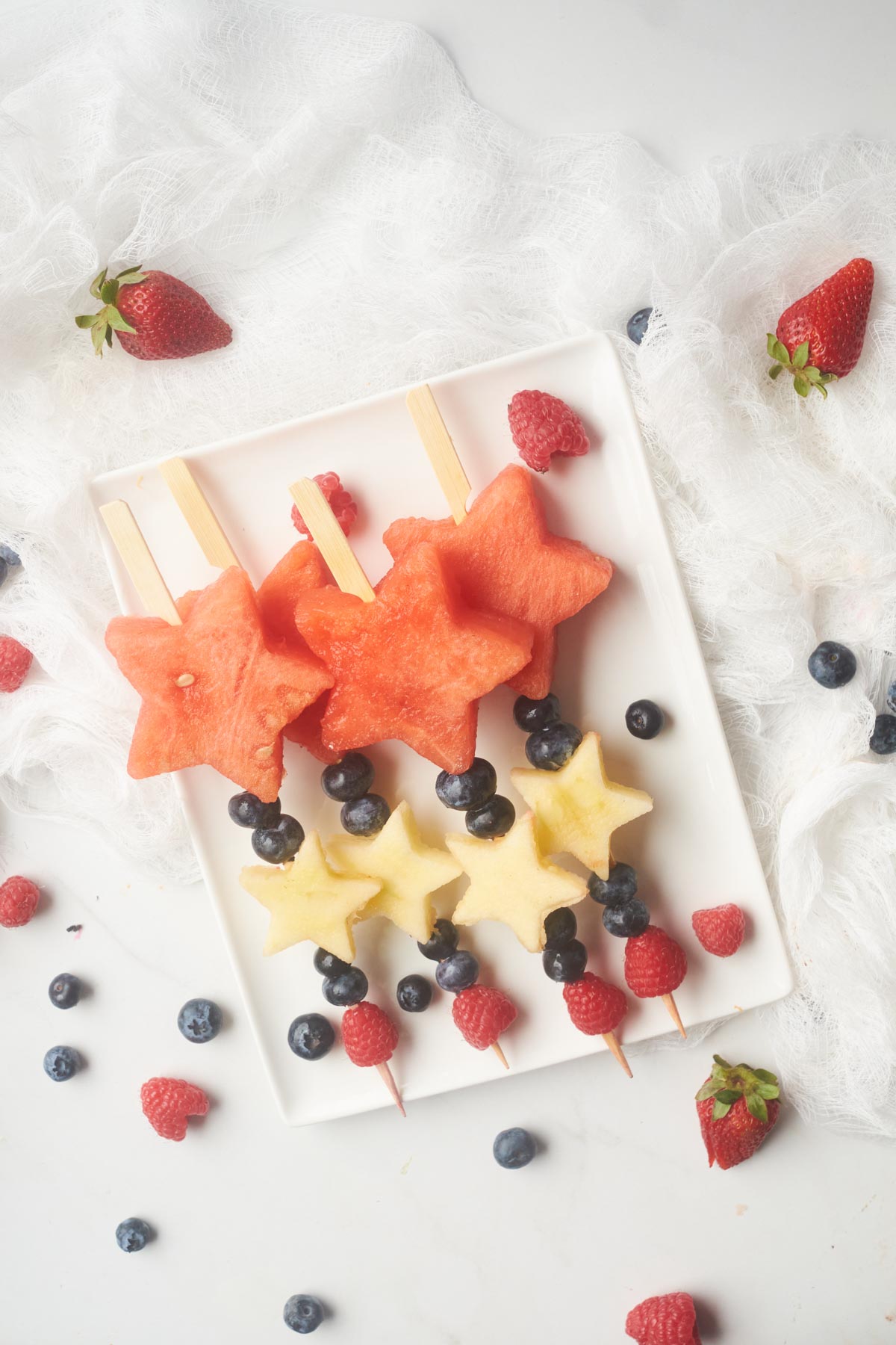 plateful of fourth of july fruit skewers with star shaped watermelon slices, berries and star shaped apple slices