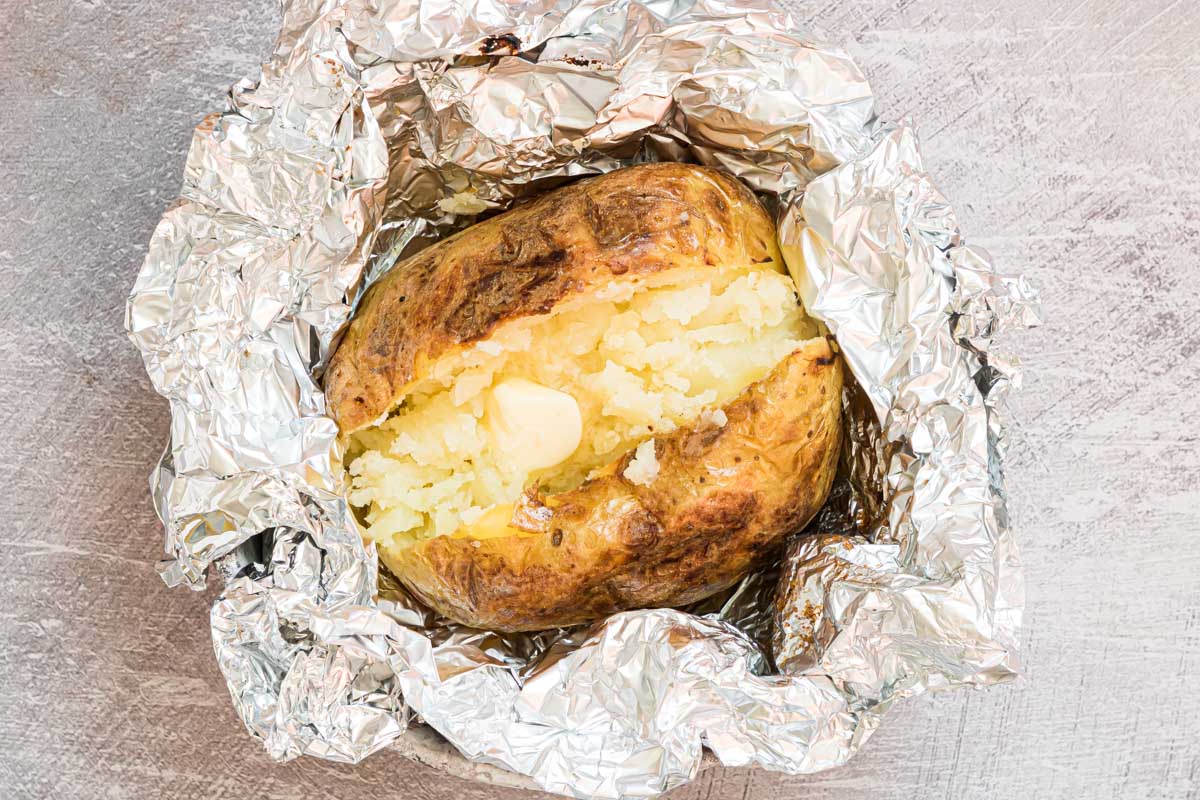 close up view of a baked potato on the grill inside aluminum foil