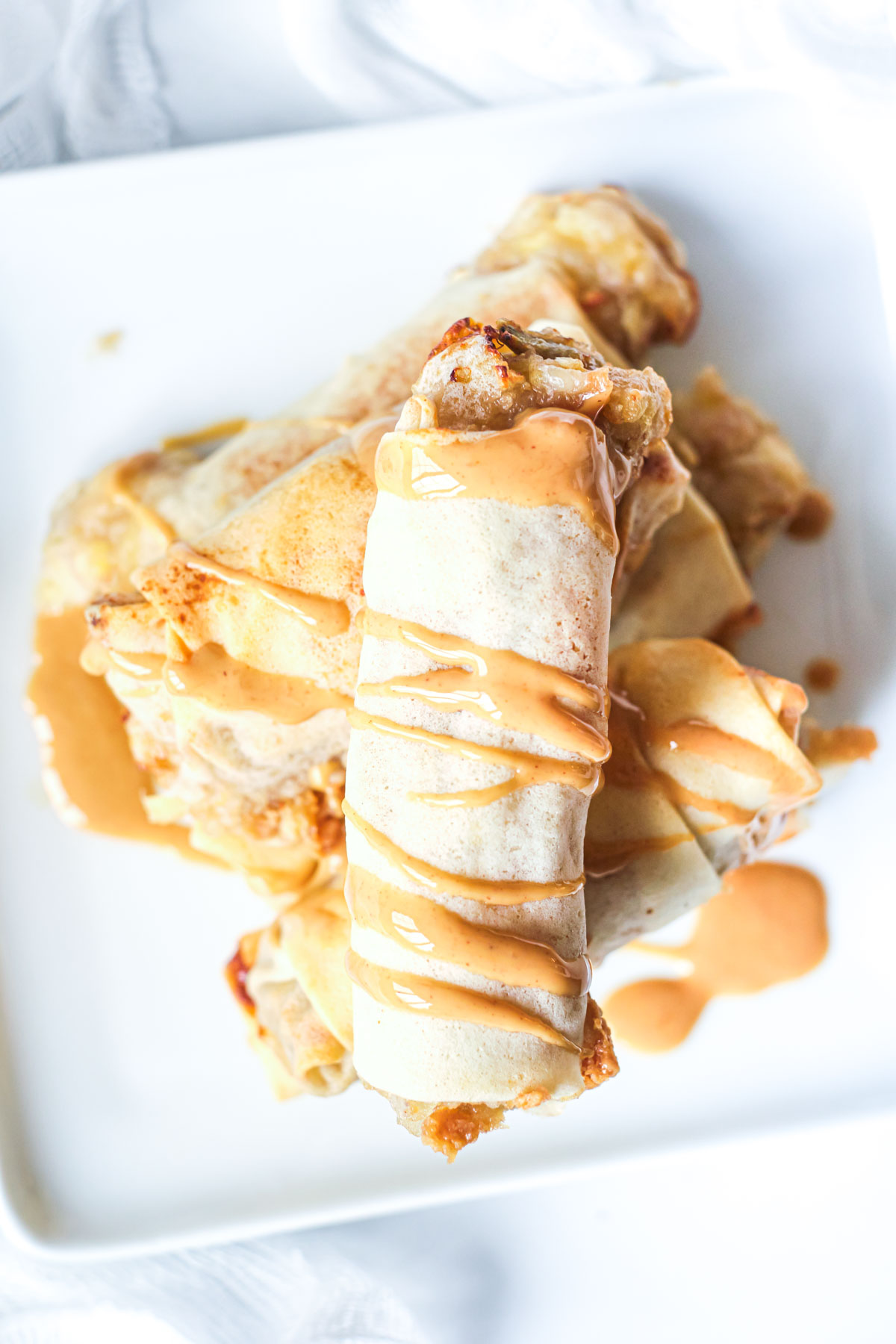 a pile of air fryer banana spring rolls with peanut butter sauce drizzles on