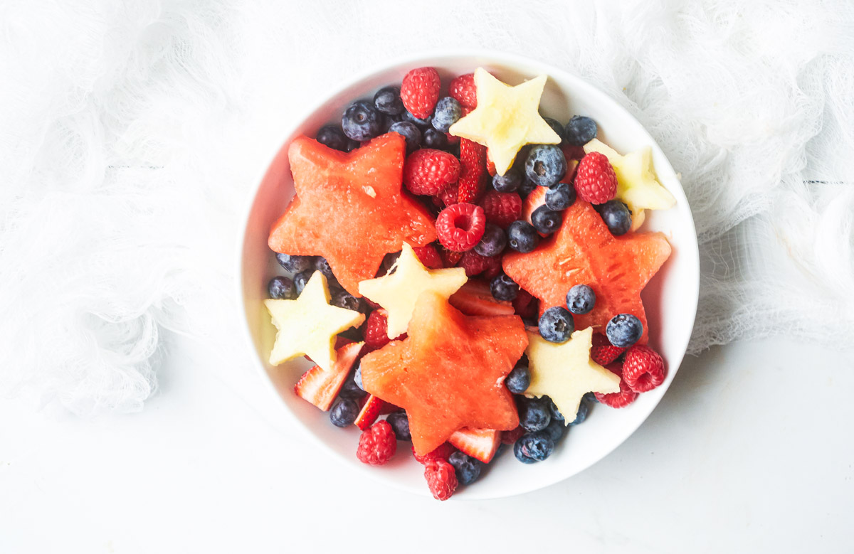 horizontal view of red white and blue fruit salad with star shaped melon and star shaped apple slices in a bowl