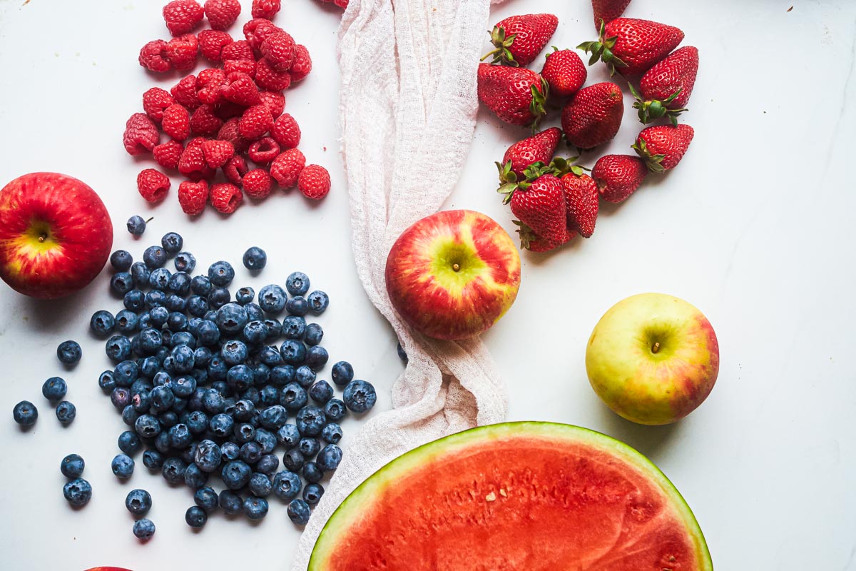 fresh fruit - watermelon, blueberries, strawberries, raspberries, and apples on. table for making patriotic fruit salad