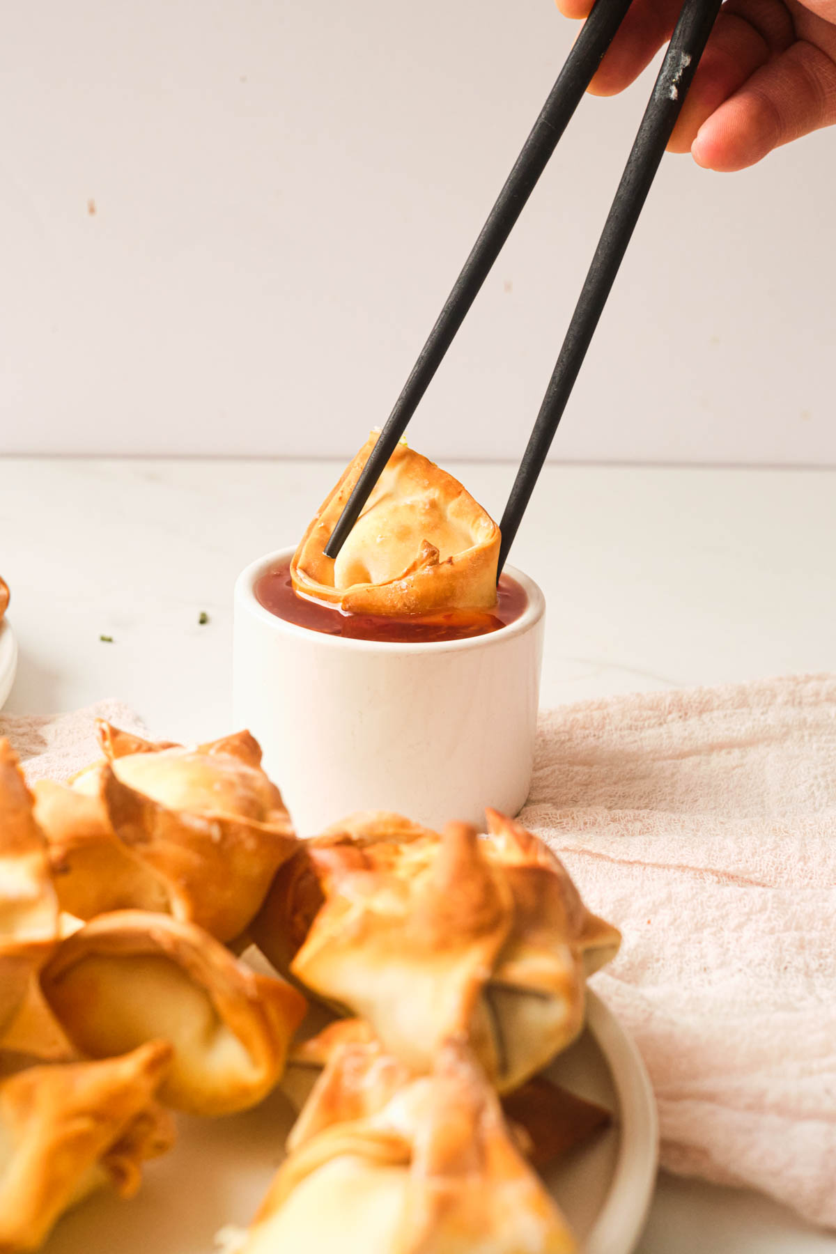 chopsticks dipping one of the air fryer wontons into a cup of sauce
