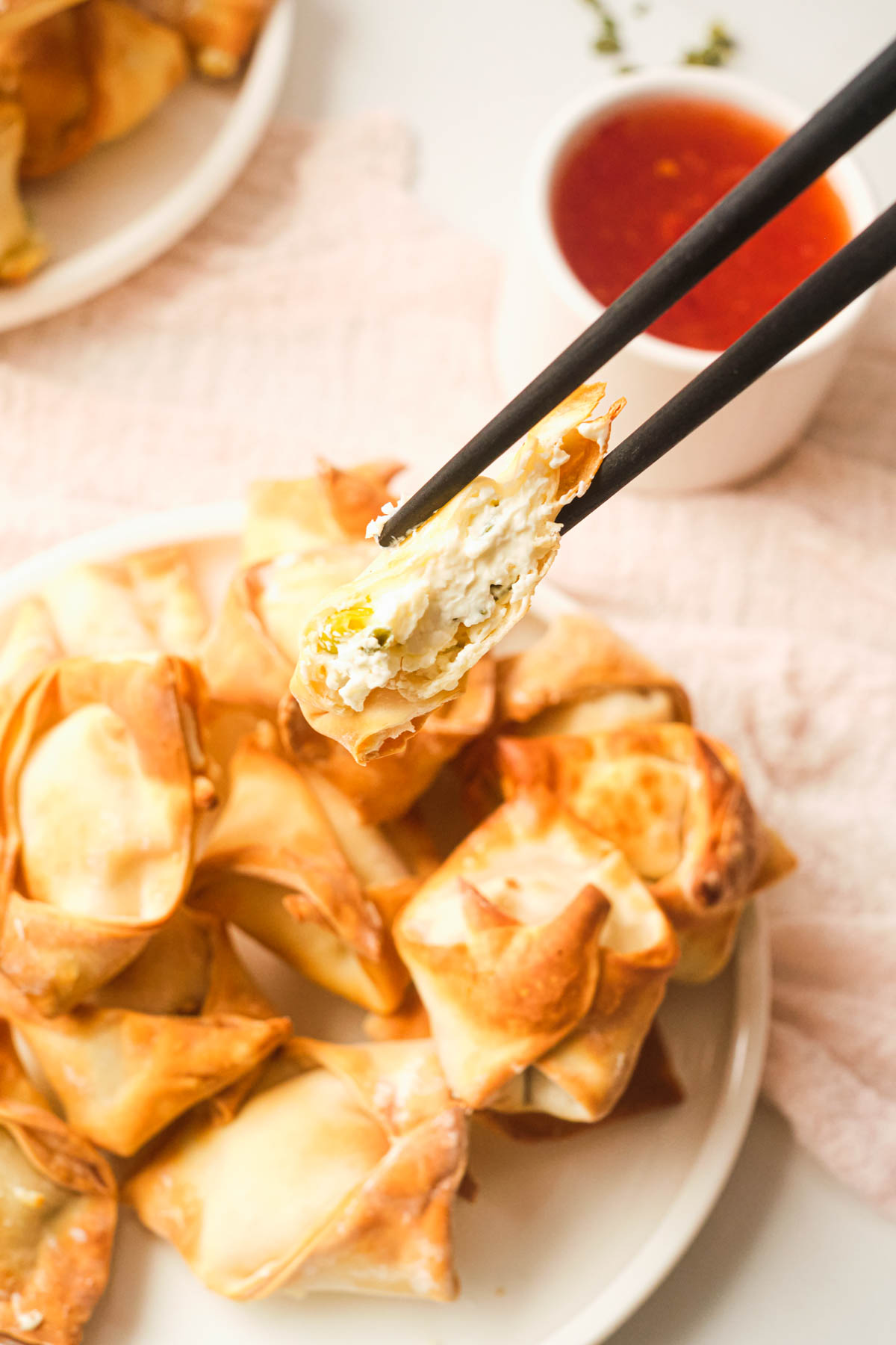 chopsticks removing a piece of air fryer wontons from a white plate