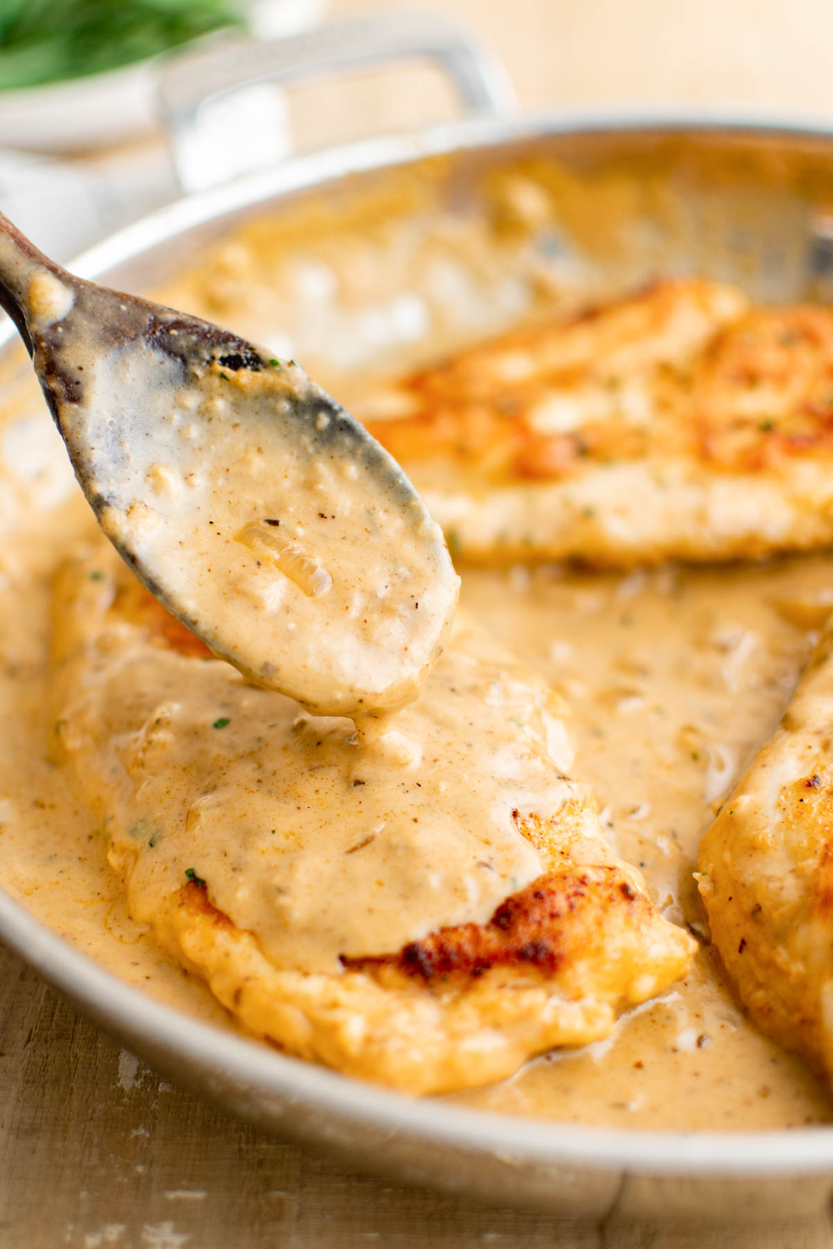 a spoon pouring gravy on top of the cooked smothered chicken in the skillet