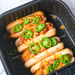 close up of cooked chili sheese dogs in an air fryer basket with jalapeno