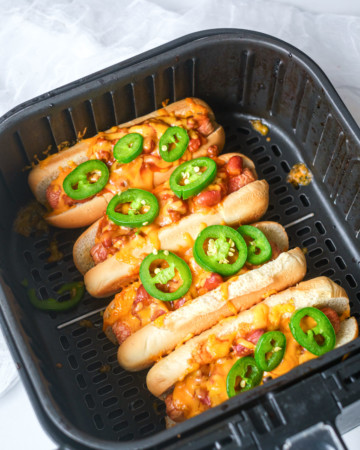 close up of cooked chili sheese dogs in an air fryer basket with jalapeno