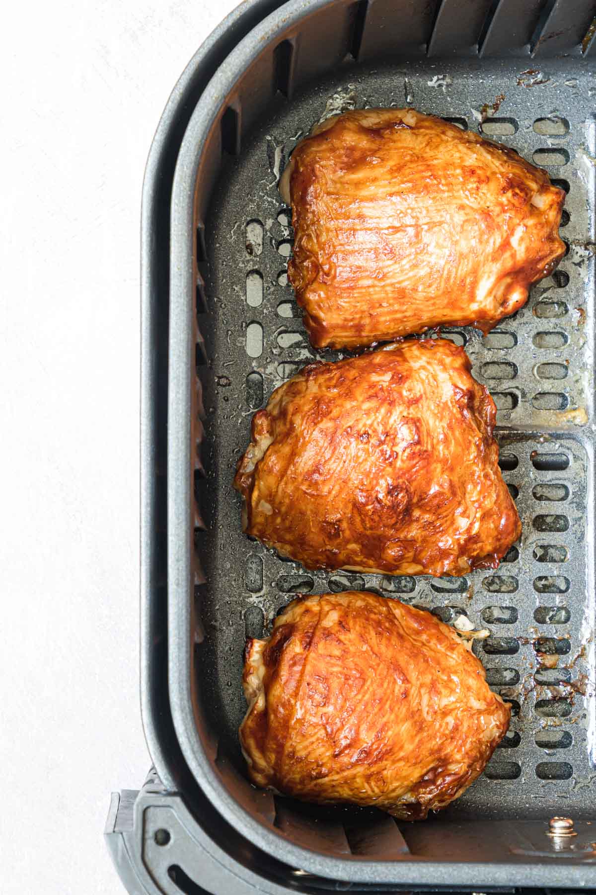 close up view of 3 frozen chicken thighs in air fryer basket