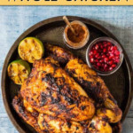A GRILLED WHOLE CHICKEN ON A PLATE WITH A SIDE OF LIME AND POMEGRANATE SEEDS