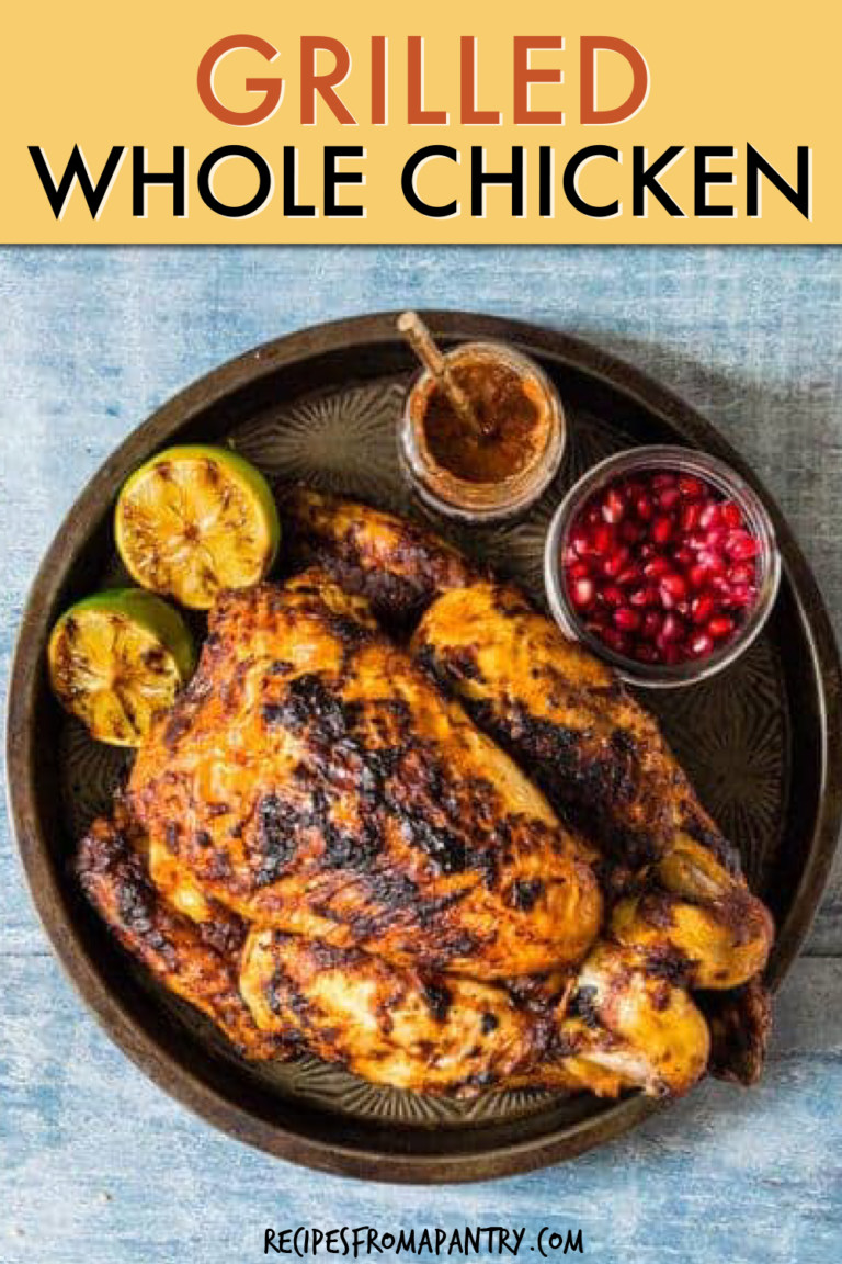 A GRILLED WHOLE CHICKEN ON A PLATE WITH A SIDE OF LIME AND POMEGRANATE SEEDS
