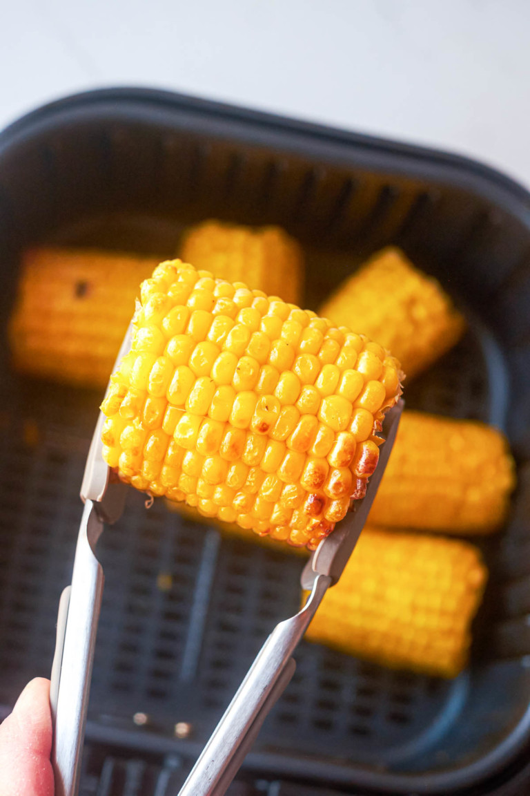 one piece of frozen corn on the cob in air fryer held by tongs