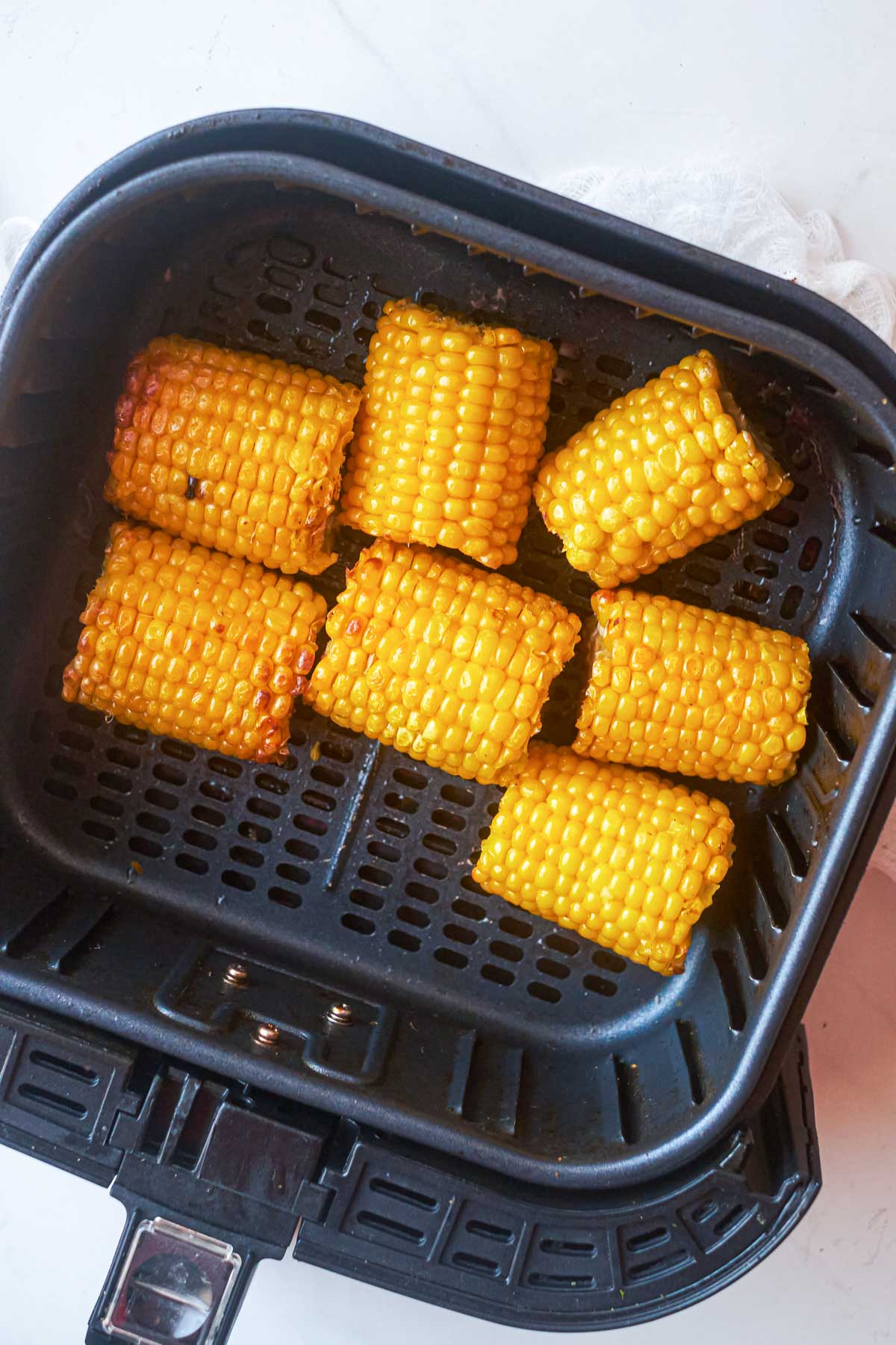 Top-down view of frozen corn on the cob in an air fryer basket