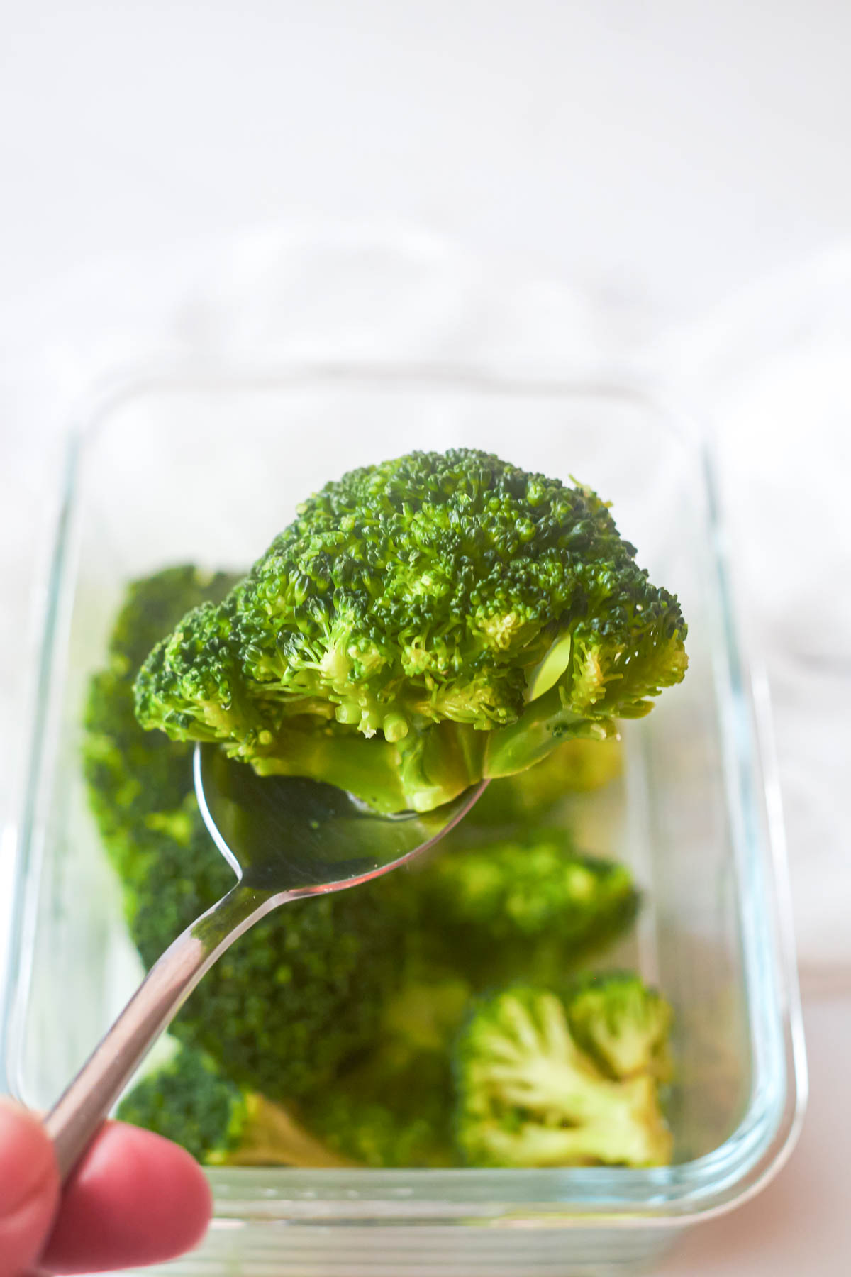a spoon removing one broccoli floret from a glass container of steamed broccoli