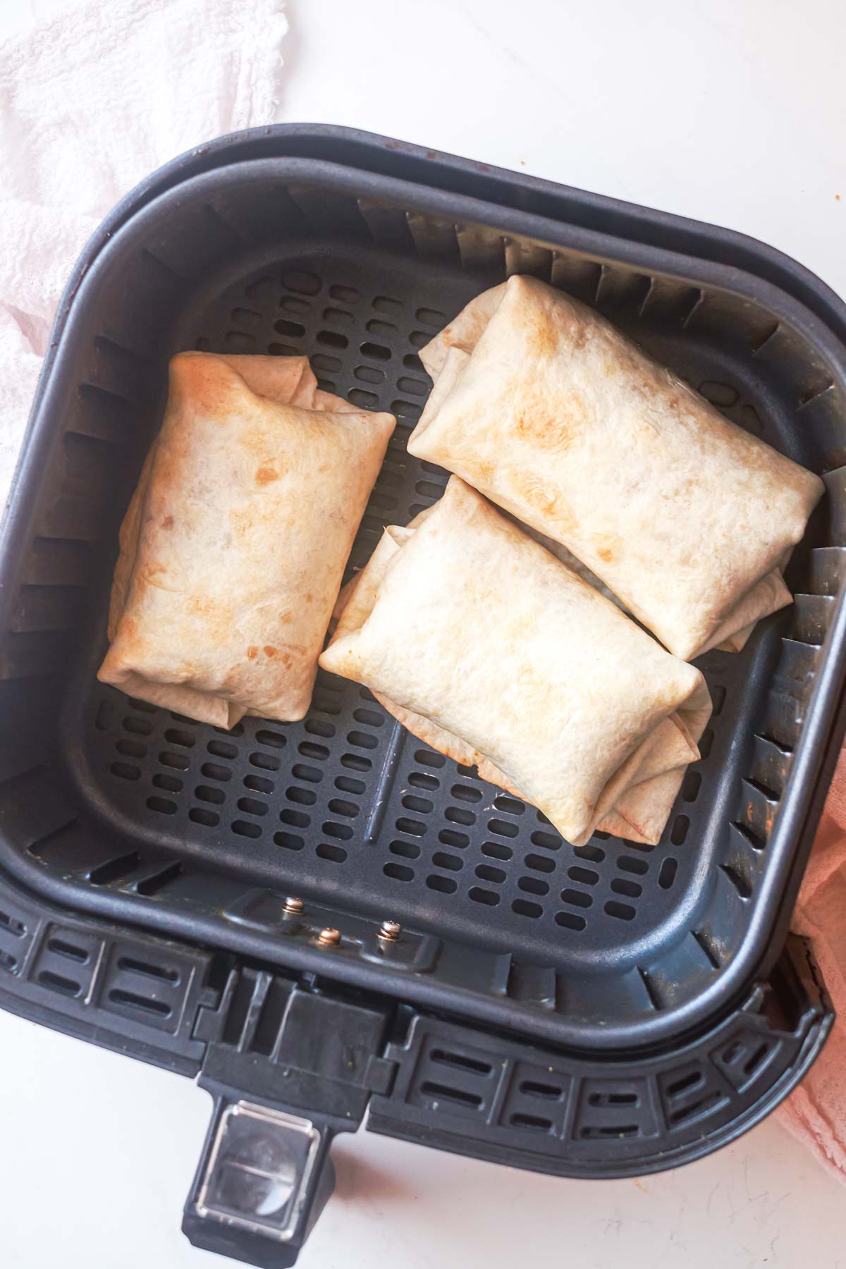 top down view of 3 air fryer burritos inside the air fryer basket