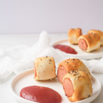 the finished air fryer sausage rolls on a white plate with ketchup for dipping