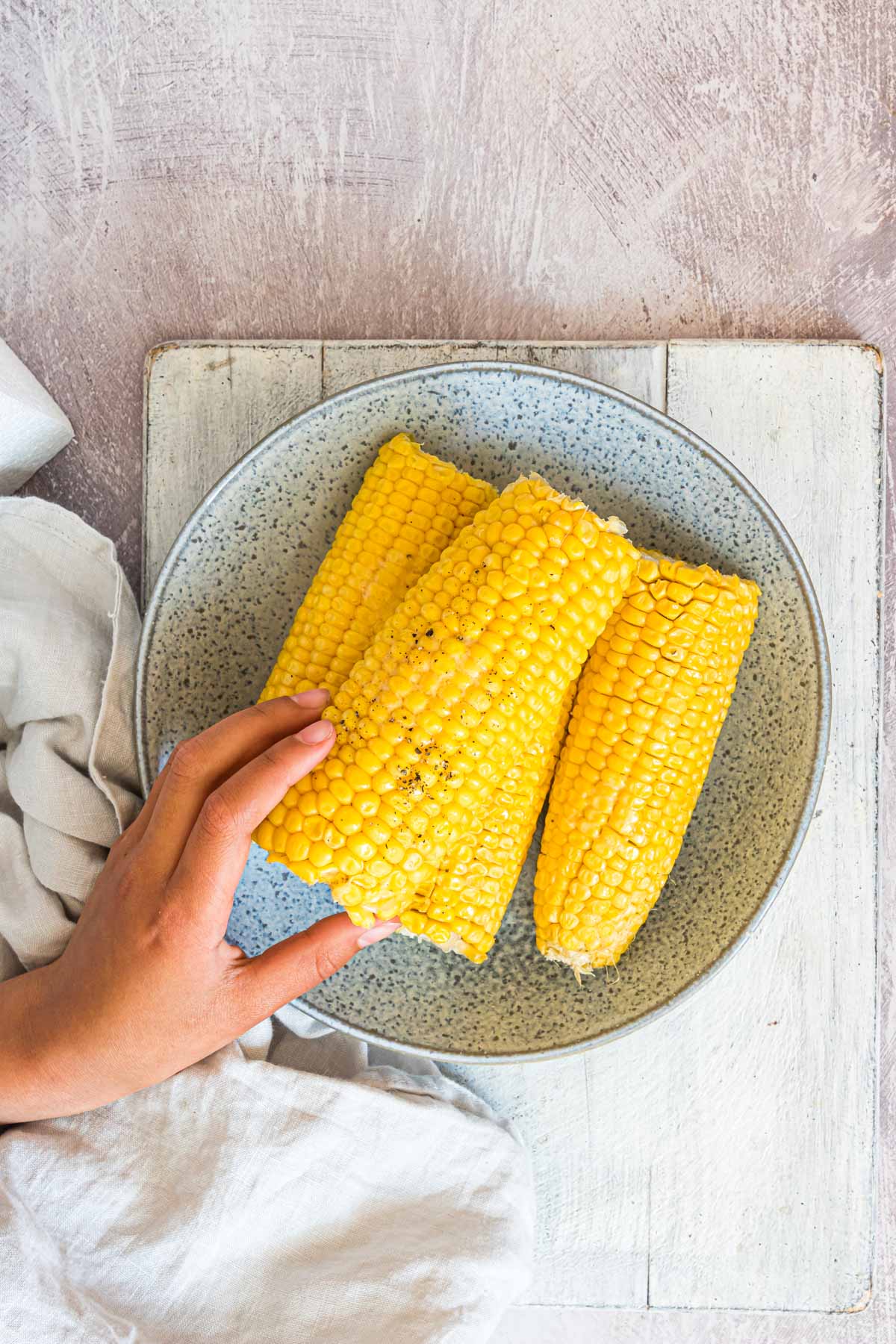 a hand reaching for one of the pieces of boiled corn on the cob