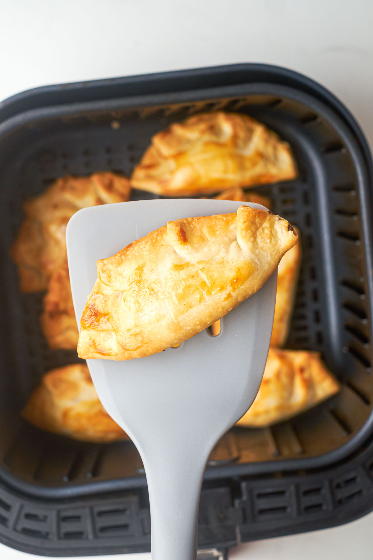 a spatula removing one of the finished air fryer frozen empanadas