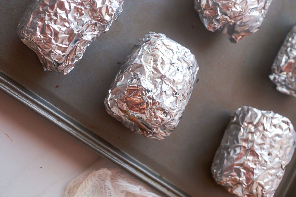 close up view of the wrapped pieces of corn on the cob in the oven