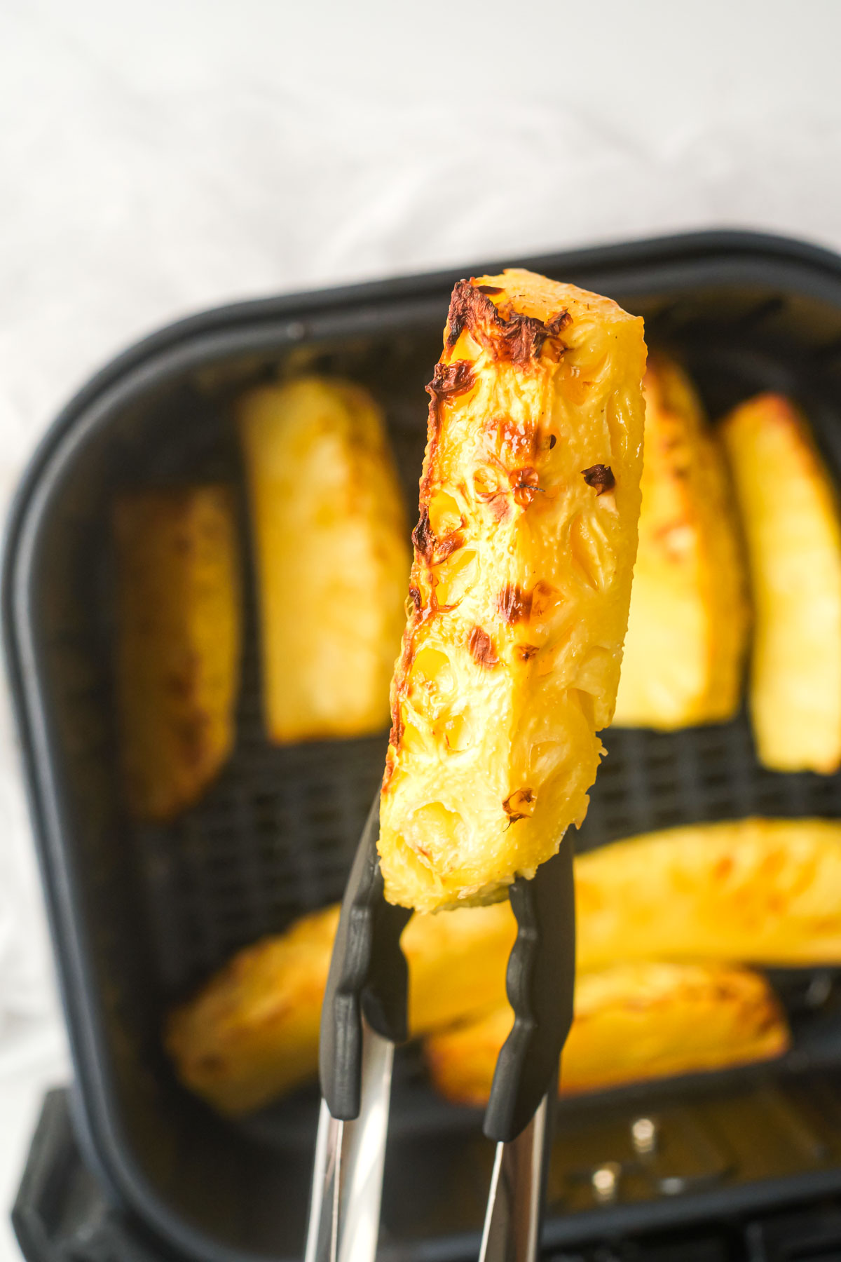 one piece of air fryer pineapple held with tongs