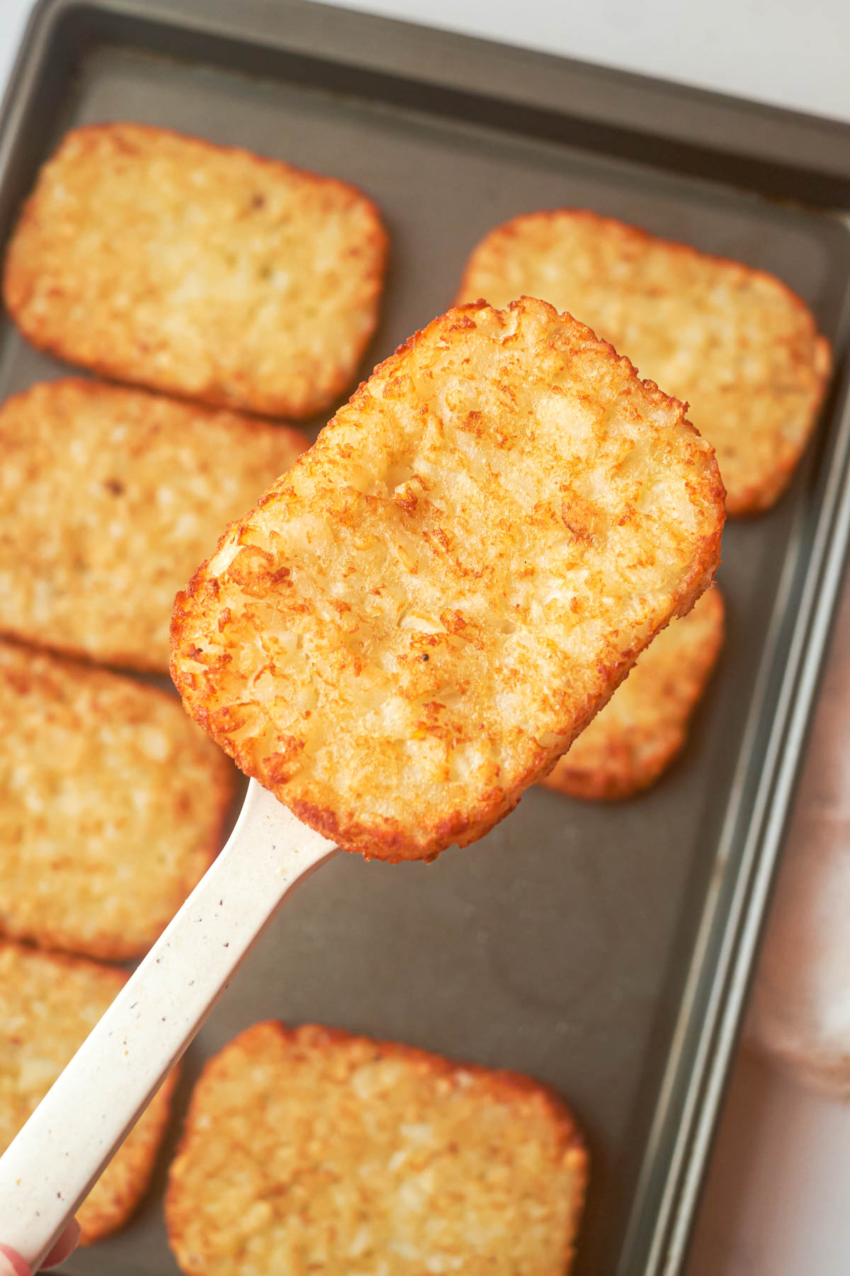 a spatula removing one of the frozen hash browns in oven from the baking sheet