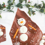 a hand holding one piece of melted snowman chocolate bark