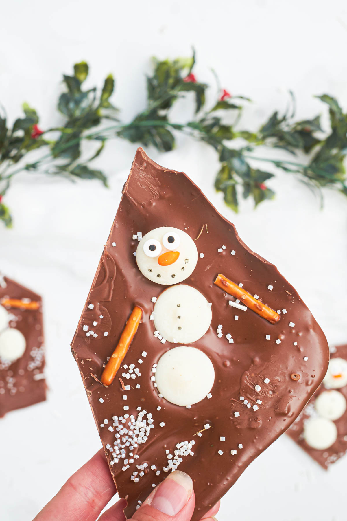a hand holding one piece of melted snowman chocolate bark