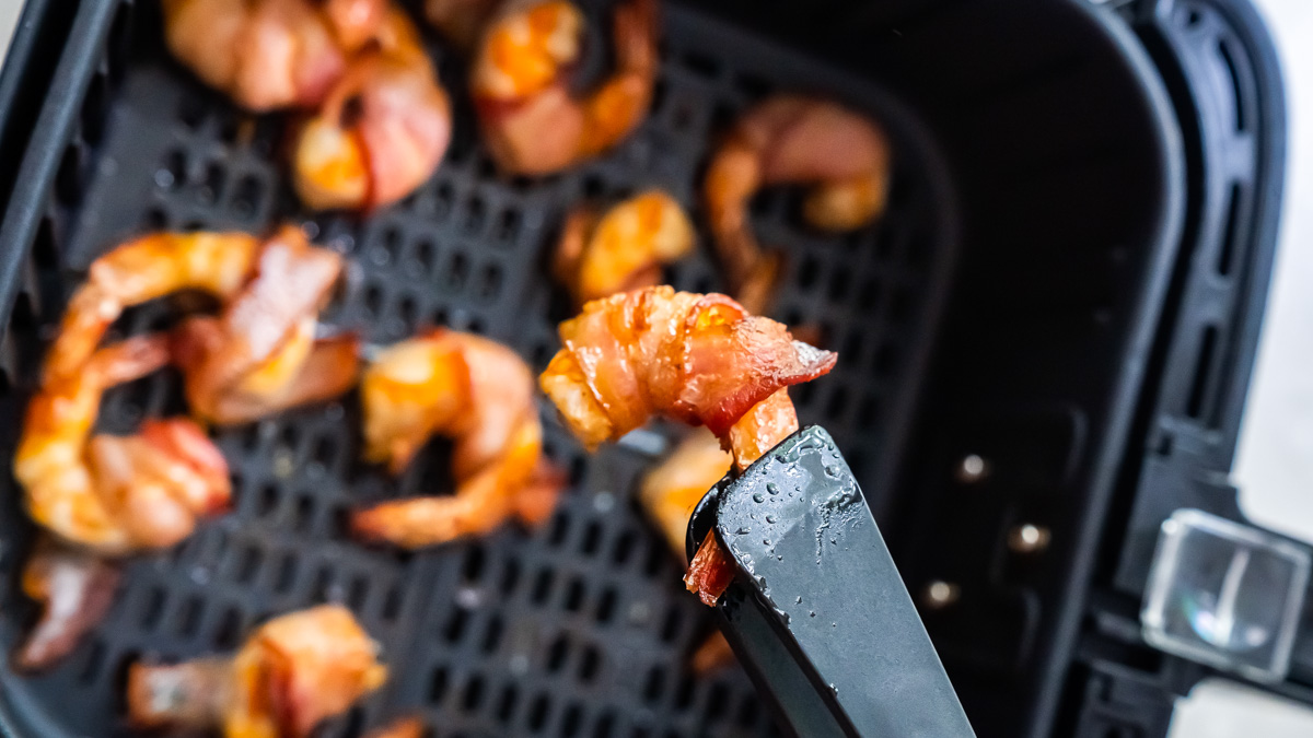 one bacon wrapped shrimp being removed from the air fryer basket