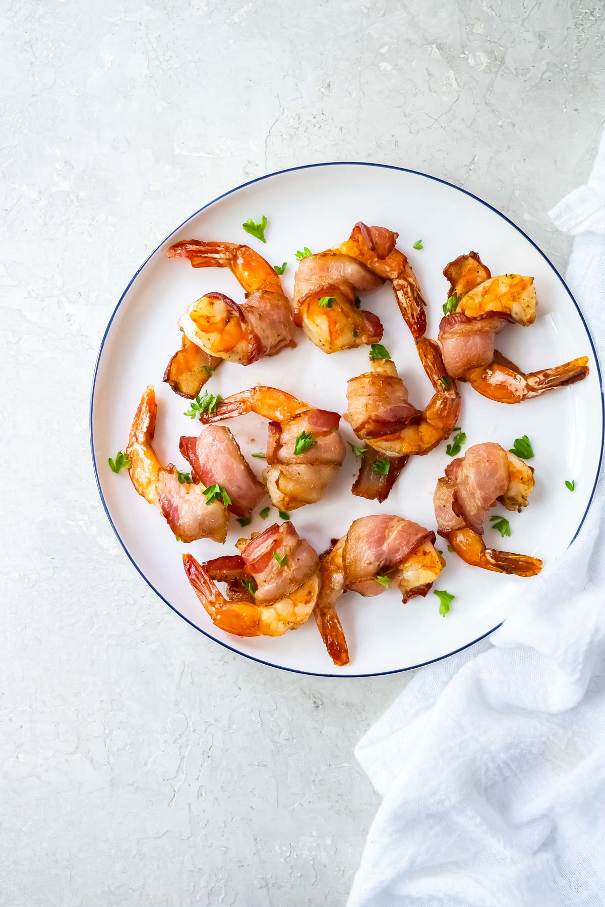 the completed bacon wrapped shrimp air fryer recipe ready to serve on a white plate with cloth napkin