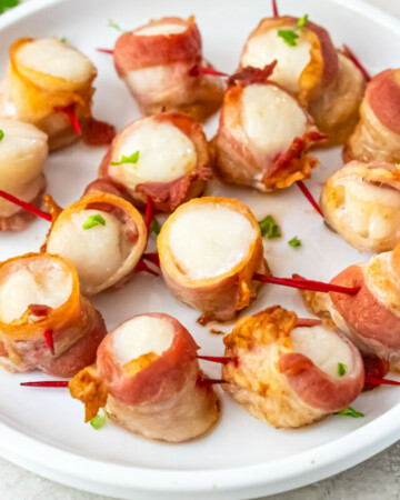 the finished air fryer bacon wrapped scallops on a white plate and garnished with parlsey