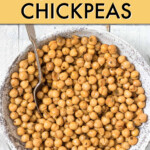 A bowl of cooked chickpeas with a spoon in it.