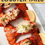 four cooked lobster tails on a plate with lemon wedges