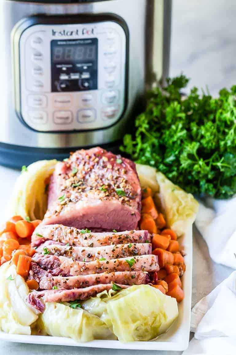 Instant Pot Corned Beef and Cabbage ready to serve on a white platter with parsley and carrots