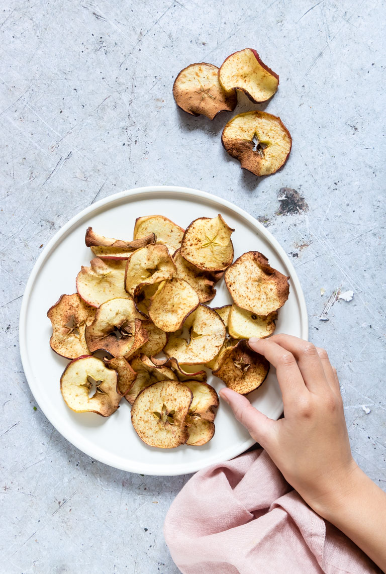 a kids hand removing one apple chip from a plate filled with air fryer apple chips