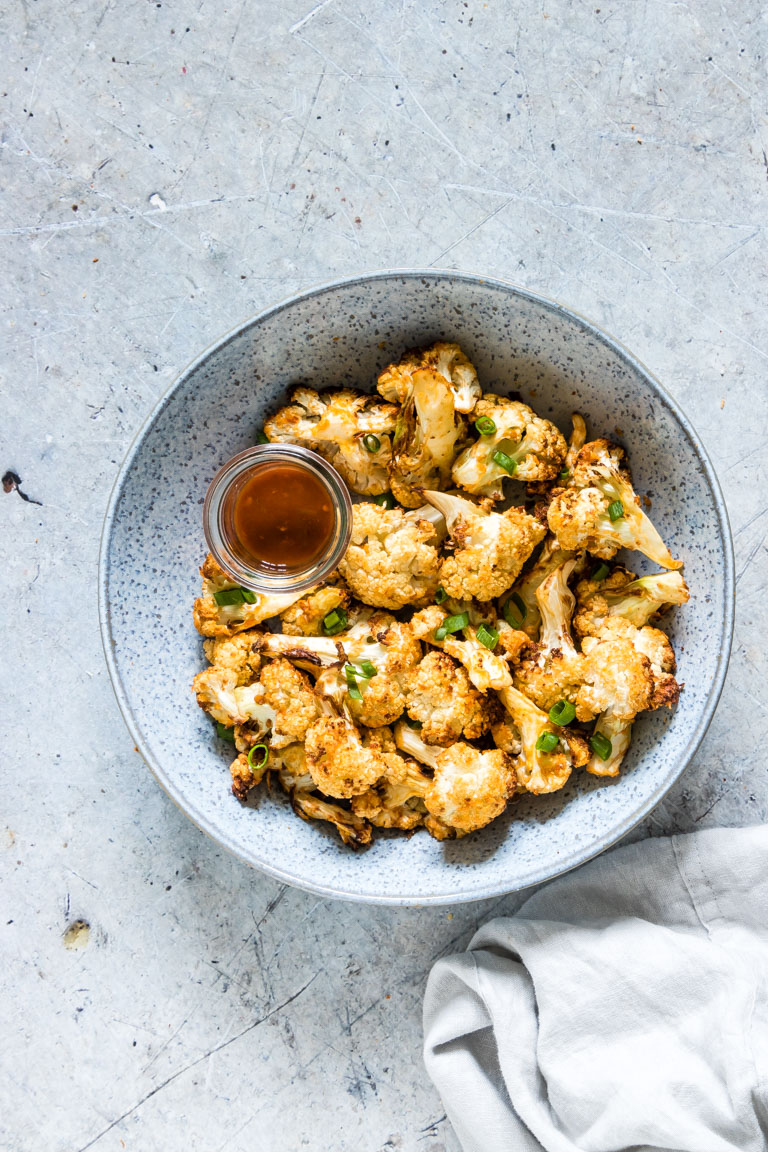 the finished cauliflower wings served in a bowl with a cup of buffalo sauce