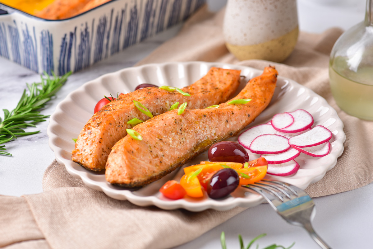 a dinner plate filled with baked salmon, radish slices and olives