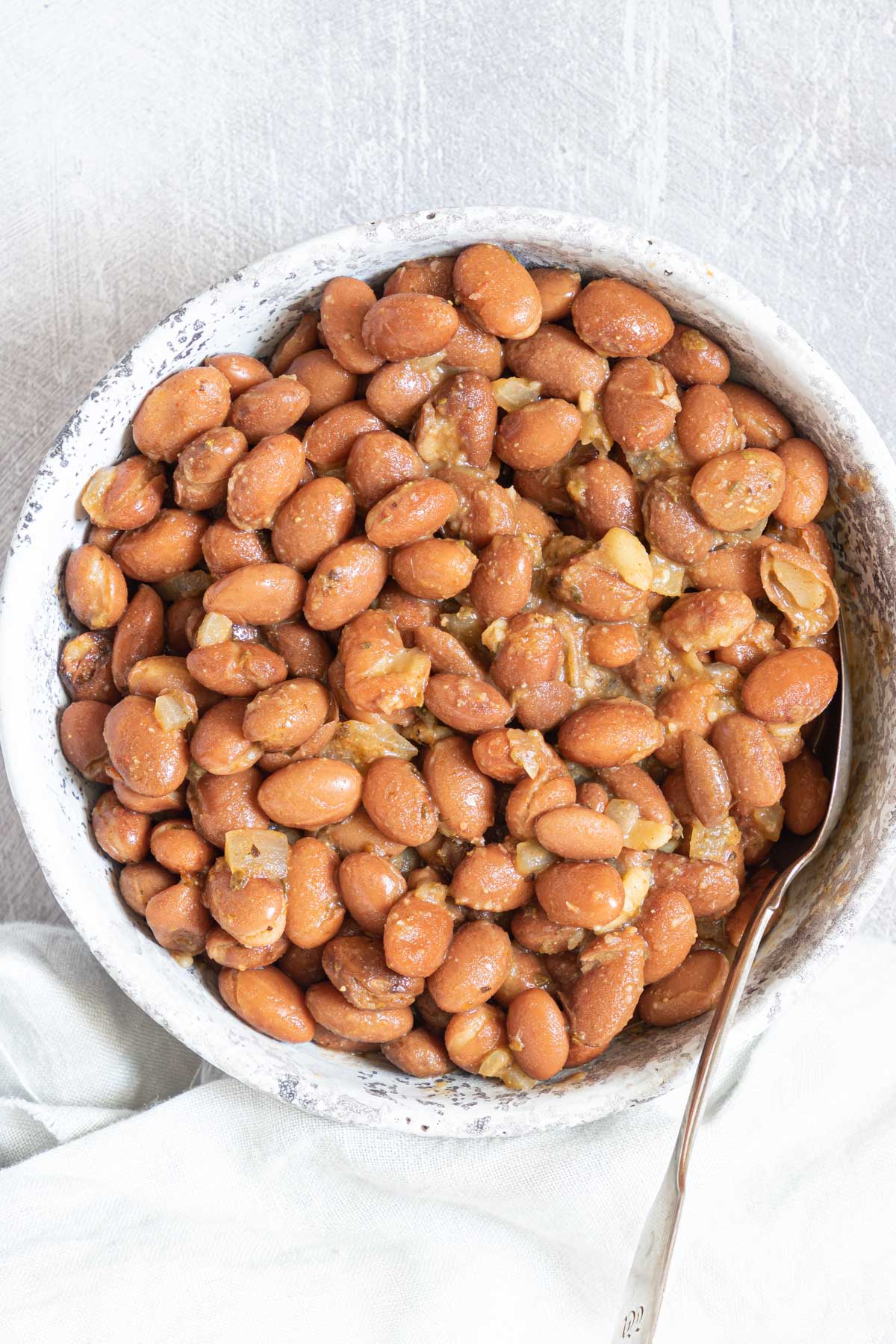 the completed how to season pinto beans recipe served in a ceramic bowl with a spoon inside