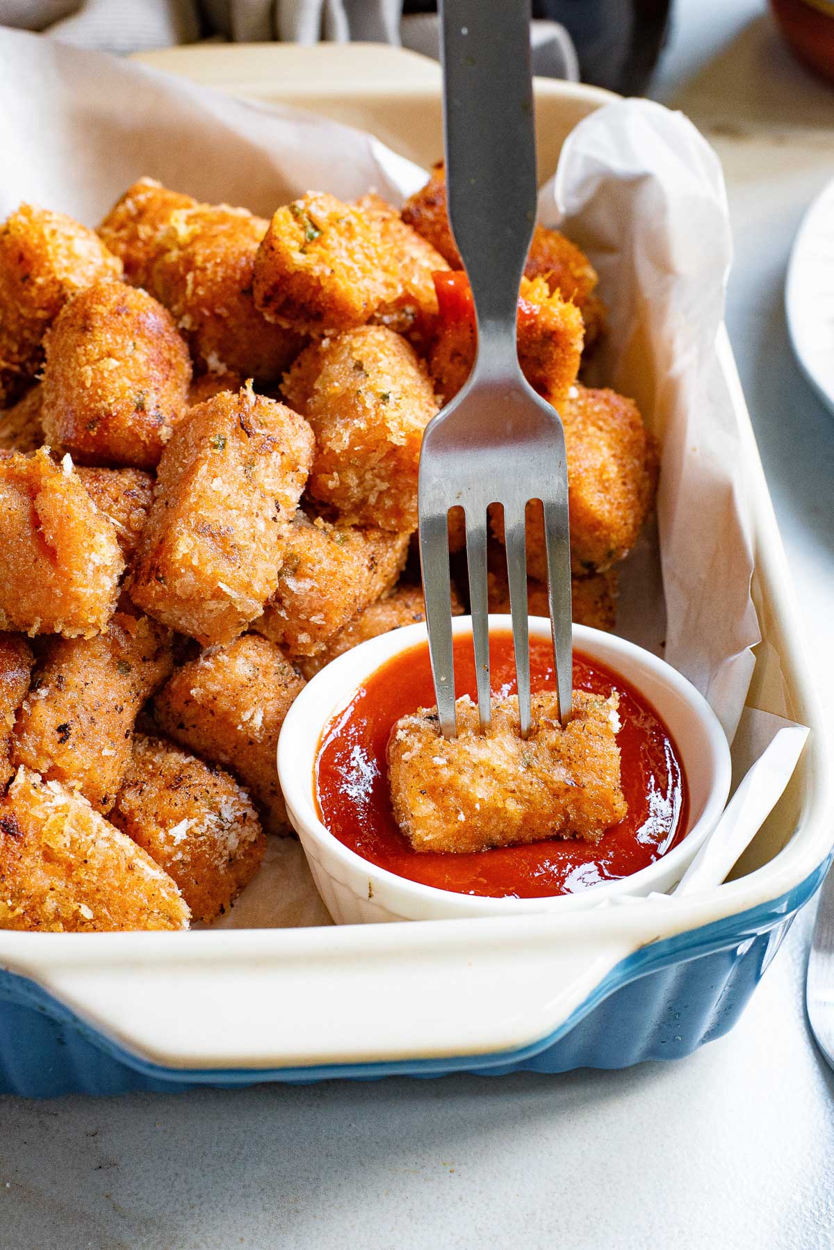 a fork dipping one of the sweet potato tater tots into ketchup