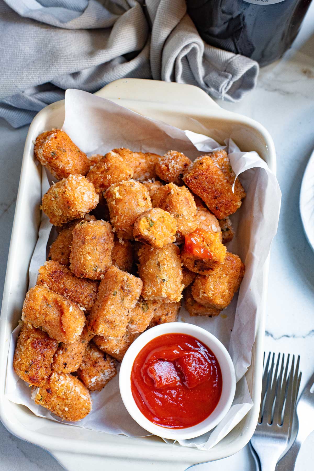 the finished sweet potato tater tots recipe served in a white dish with a side of sauce