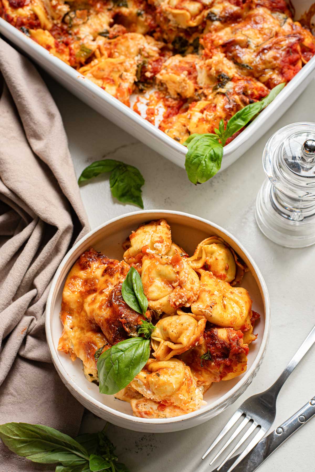 a bowl filled with baked tortellini sitting next to the casserole dish