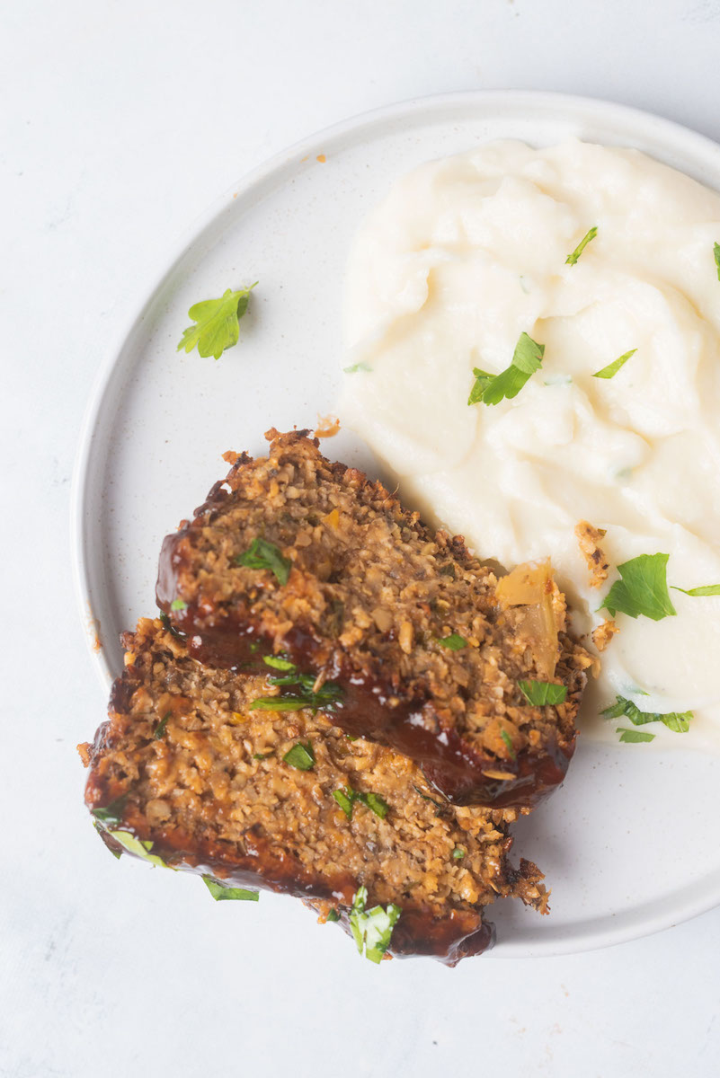 two pieces of vegan meatloaf on a plate with mashed potatoes