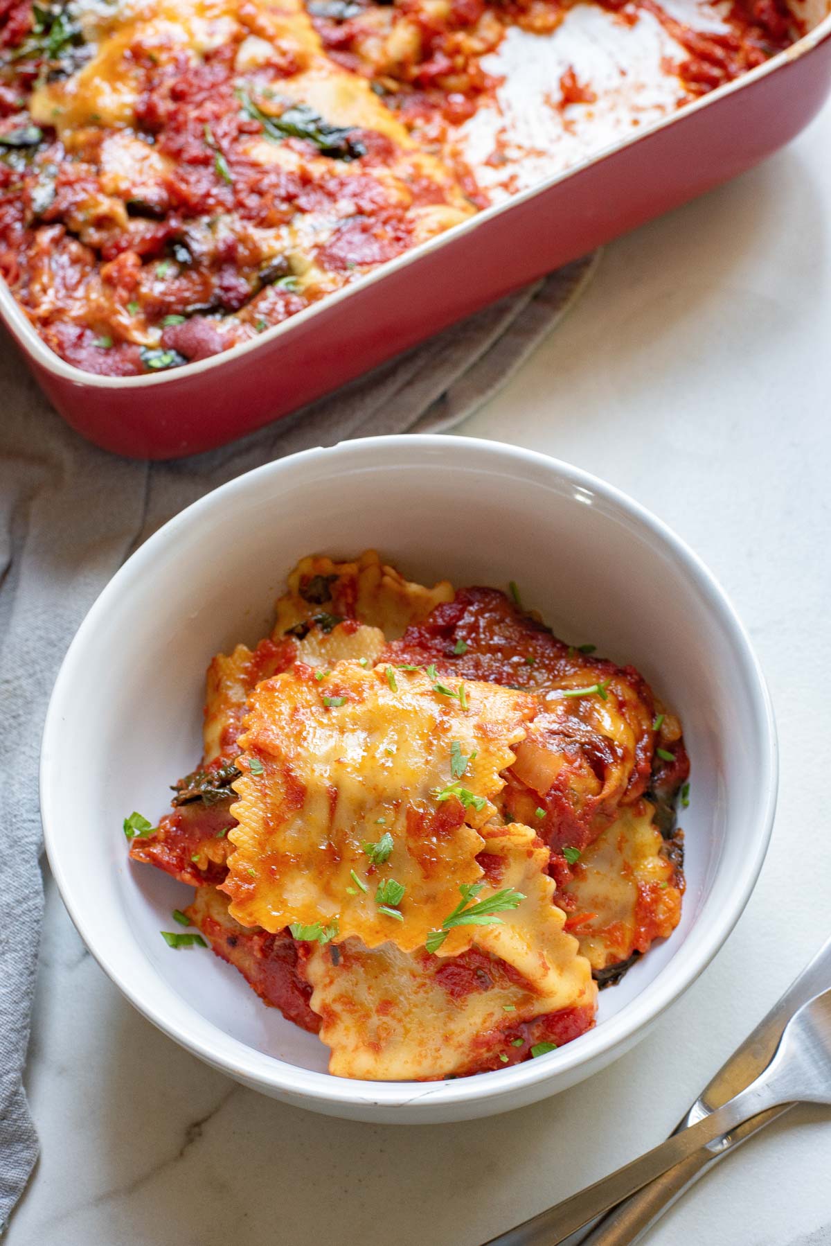 a serving of ravioli bake in a white bowl set in front of a baking dish