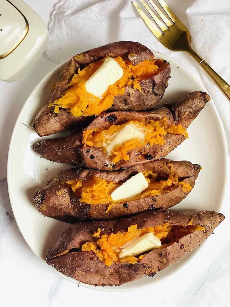 four air fryer sweet potatoes topped with butter and served on a white plate