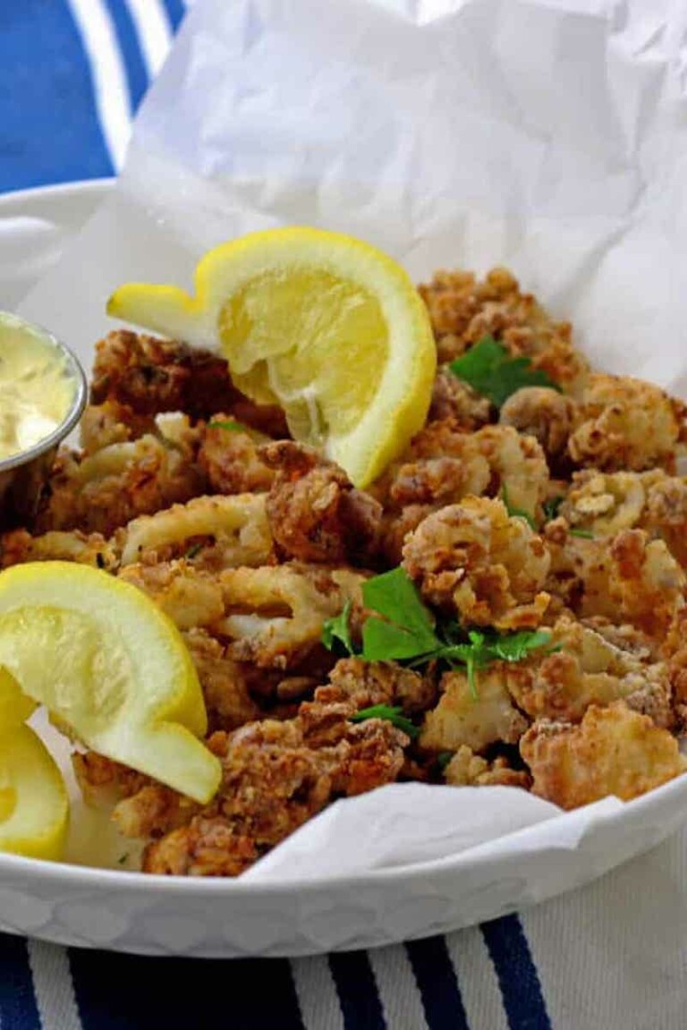 a white bowl filled with air fryer calamari and lemon wedges