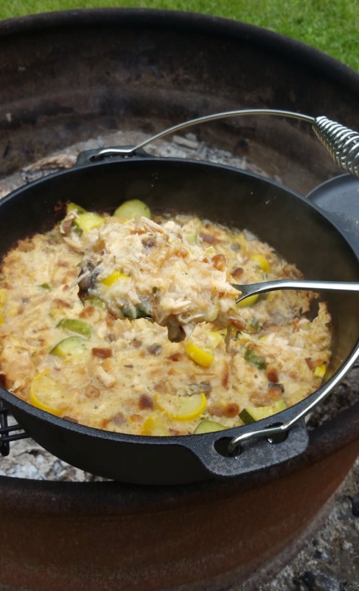 the chicken and squash dutch oven casserole being cooked over a campfire