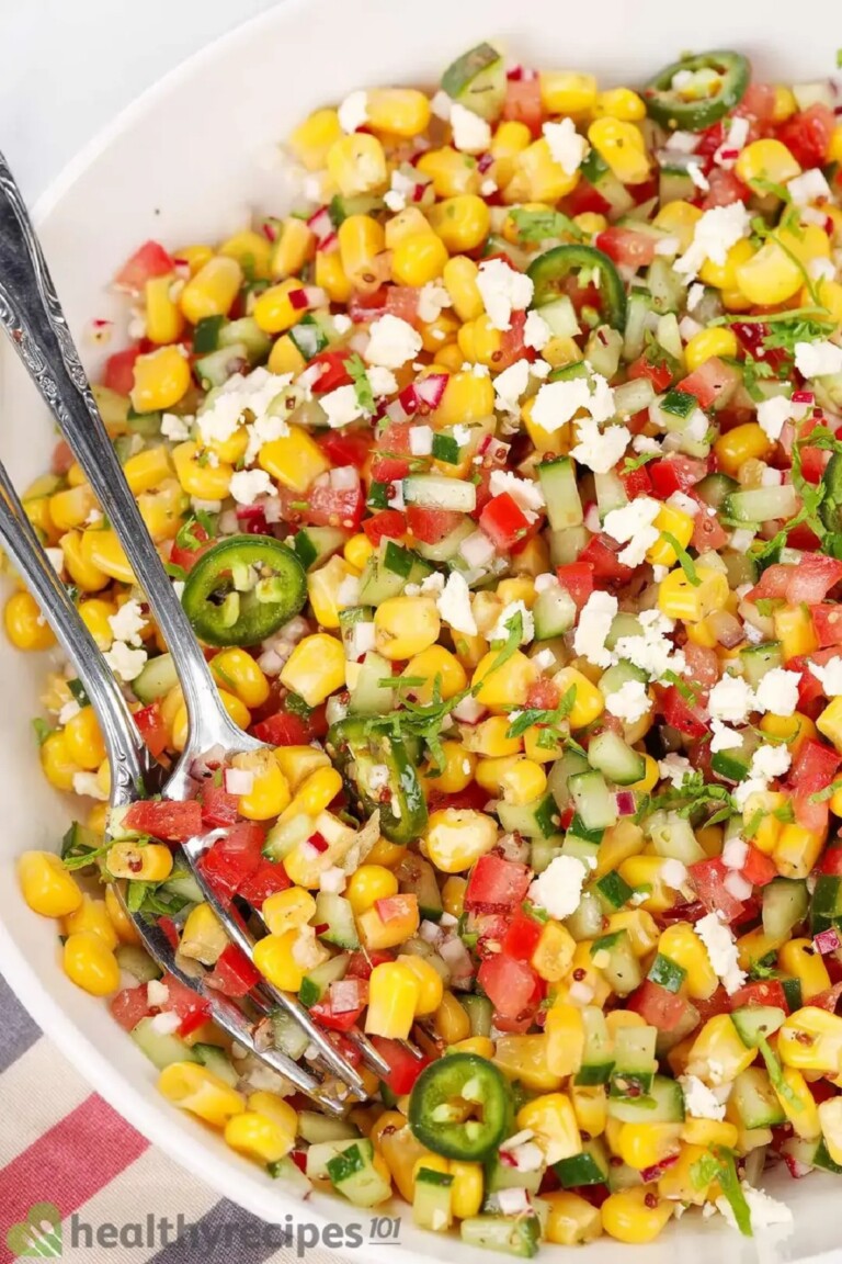 Close up image of Corn salad showing the corn and two servings spoons in a white bowl.